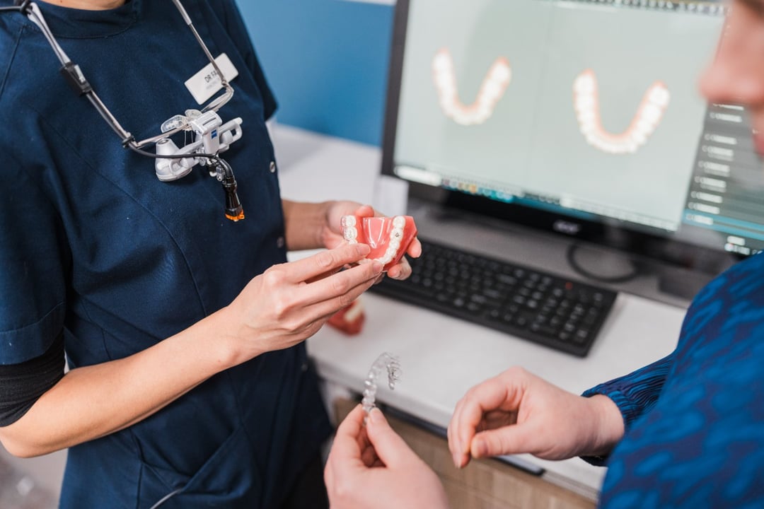 An Innova Dental dentist holding a clear aligner and a teeth model, with a digital scan of the patient's teeth on screen